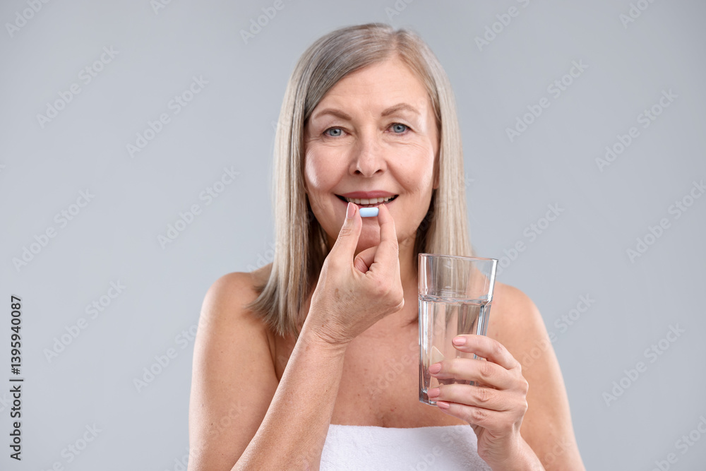 Happy woman with glass of water taking collagen pill on grey background Happy woman with glass of water taking collagen pill on grey background