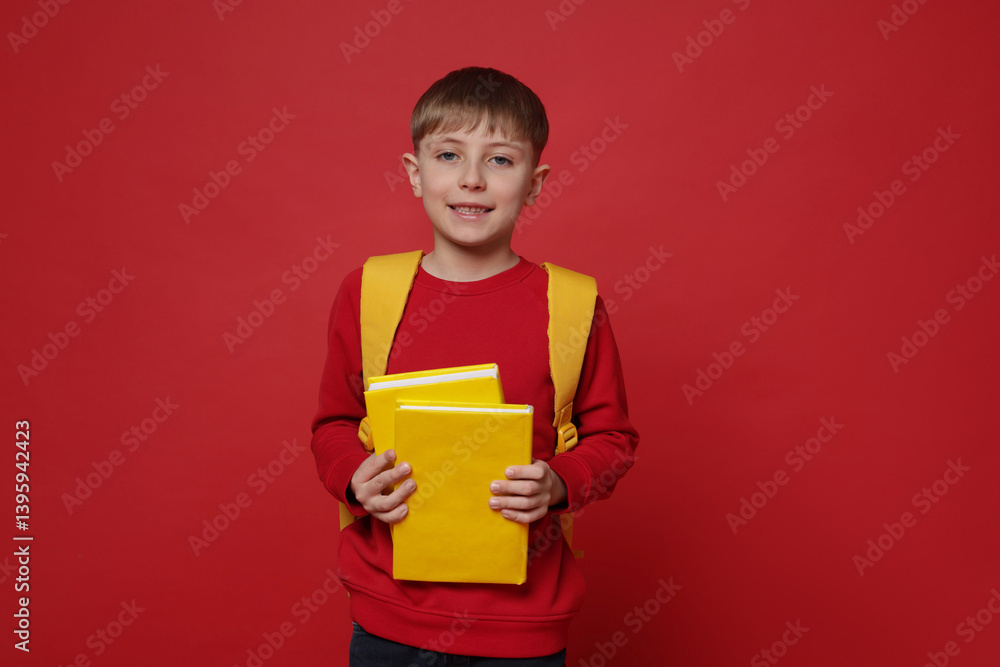 Cute schoolboy with backpack and books on red background