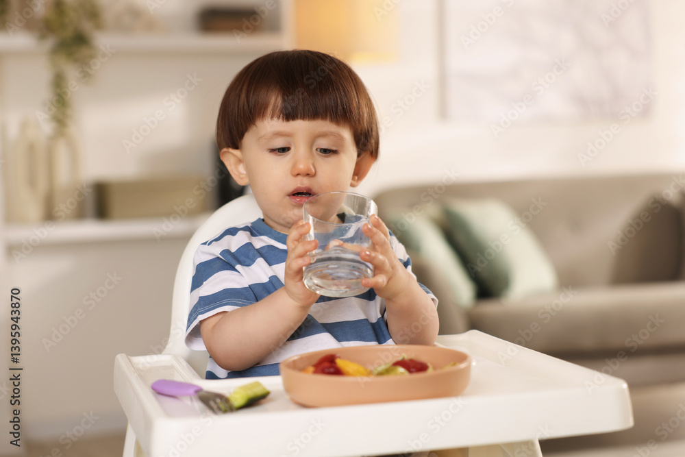 Cute little boy drinking water in high chair at home Cute little boy drinking water in high chair at home
