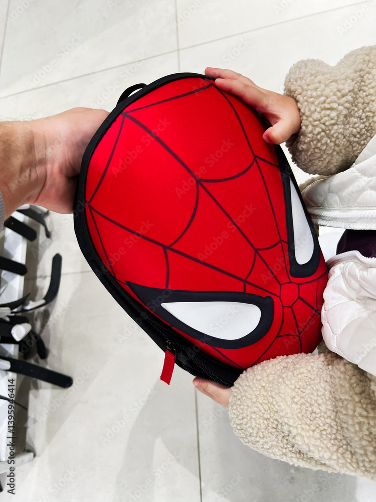 Naklejka premium Person holding a red Spider Man Spider Manthemed backpack with white eyes in a store