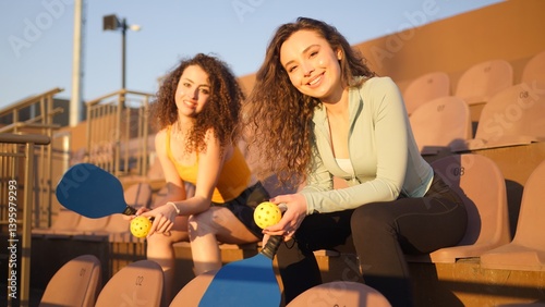 Portrait of young women adults posing with pickleball paddle and ball on stadium chairs