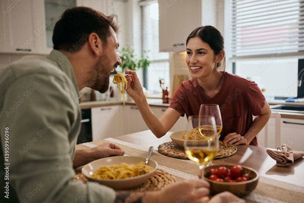 Happy woman feeding her boyfriend while eating lunch at dining table. Happy woman feeding her boyfriend while eating lunch at dining table.