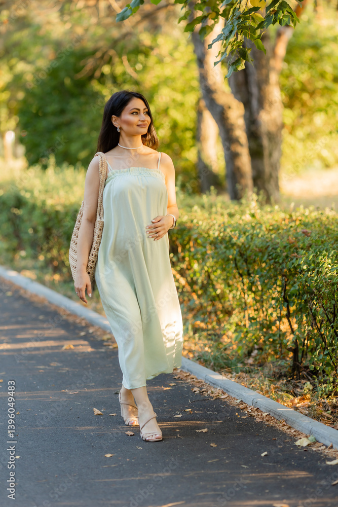 Beautiful brunette pregnant woman walks in the park at sunset in summer Beautiful brunette pregnant woman walks in the park at sunset in summer