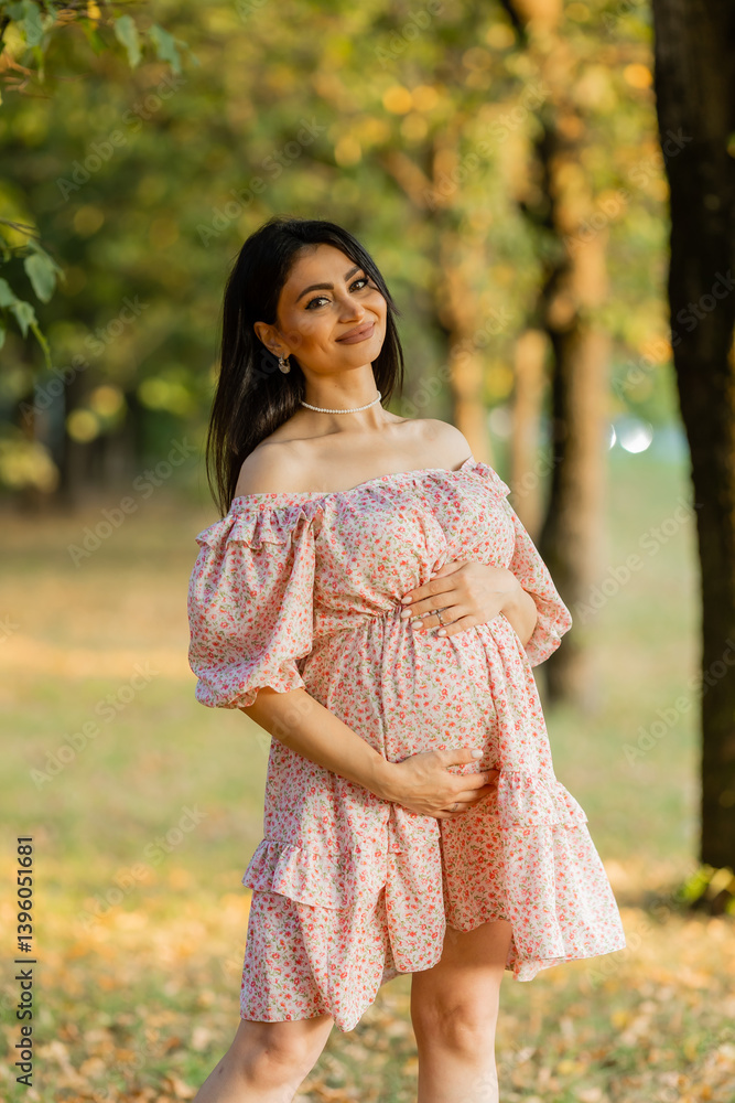 Beautiful brunette pregnant woman walks in the park at sunset in summer Beautiful brunette pregnant woman walks in the park at sunset in summer