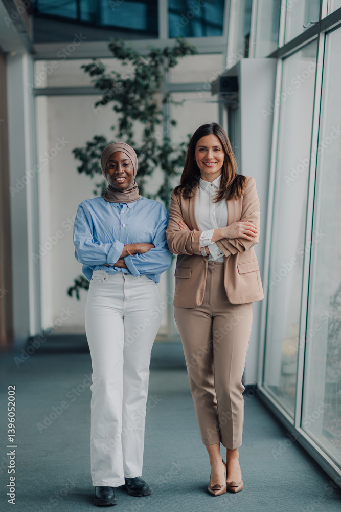 Obraz premium Two businesswomen smiling with arms crossed in modern office hallway