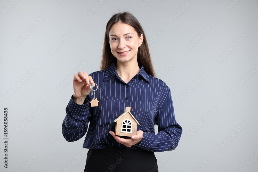 Real estate agent holding key with keychain and house model on light grey background Real estate agent holding key with keychain and house model on light grey background