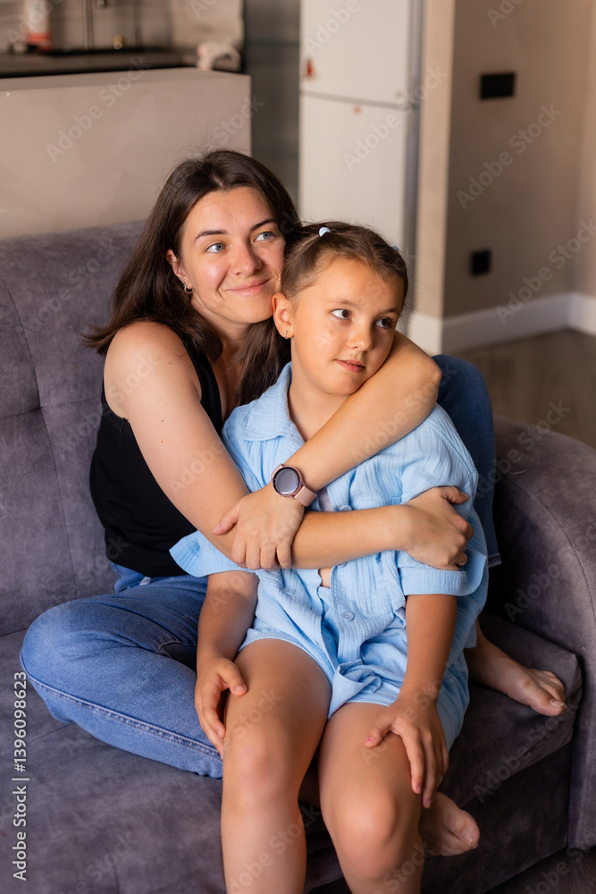 Mom and daughter are sitting at home on the couch, hugging Mom and daughter are sitting at home on the couch, hugging