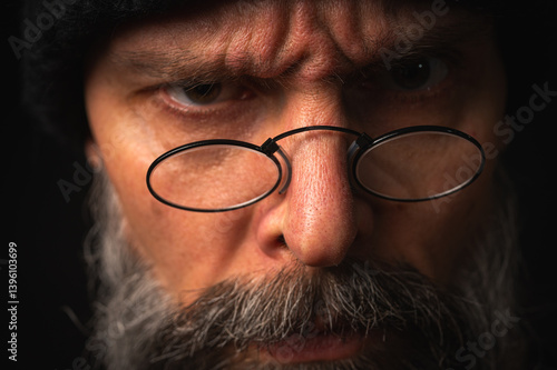 Obraz na płótnie Portrait of angry bearded man in black hat and glasses growling at camera. Dramatic portrait in subdued lighting, expressive face, emotional tension, dark background w salonie