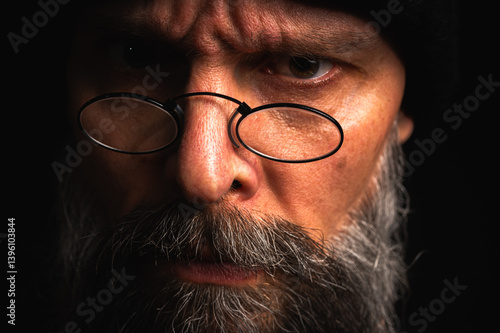 Obraz na płótnie Portrait of angry bearded man in black hat and glasses growling at camera. Dramatic portrait in subdued lighting, expressive face, emotional tension, dark background w salonie