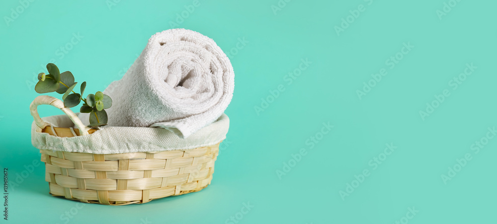 Wicker basket with clean soft towel on turquoise background with space for text