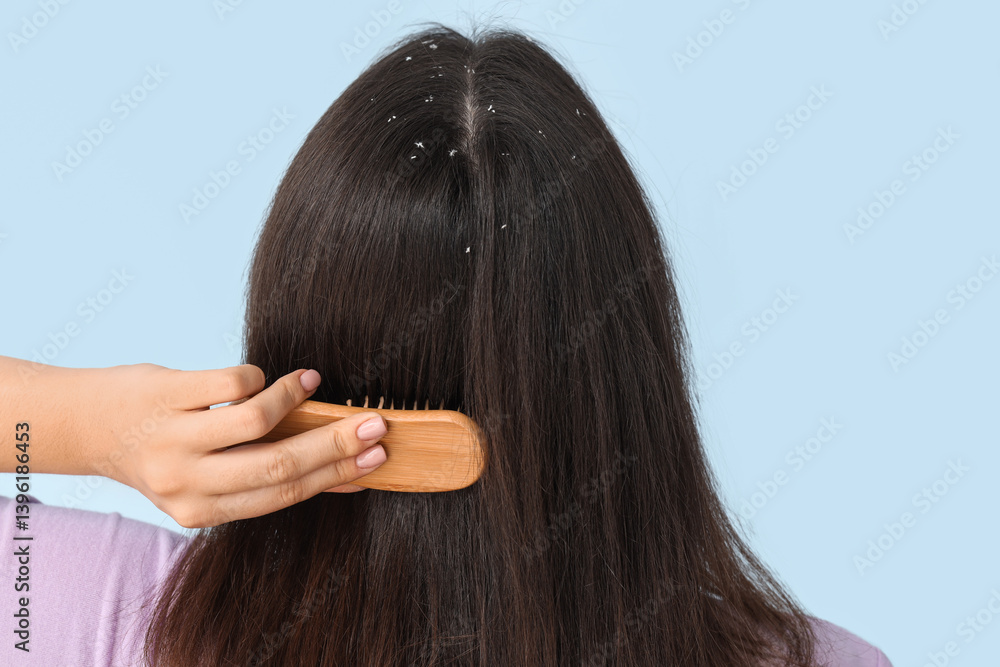 Naklejka premium Young woman with dandruff problem combing hair on blue background, back view