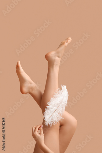 Cuadro en lienzo Legs of young woman with soft feather on brown background