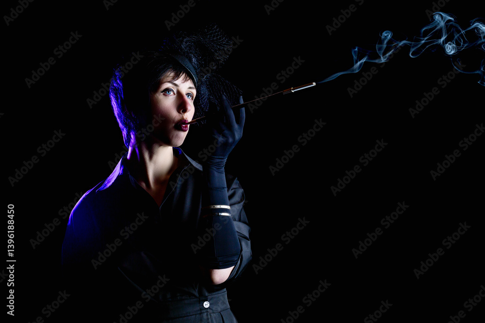 Retro noir style. Dramatic portrait of a beautiful charming brunette smoking woman in black dress with mouthpiece against black background