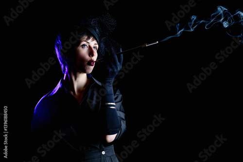 Obraz na płótnie Retro noir style. Dramatic portrait of a beautiful charming brunette smoking woman in black dress with mouthpiece against black background w salonie