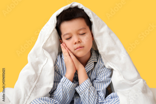 Obraz na płótnie Sleepy little Asian boy in pajamas with blanket sitting on yellow background w salonie