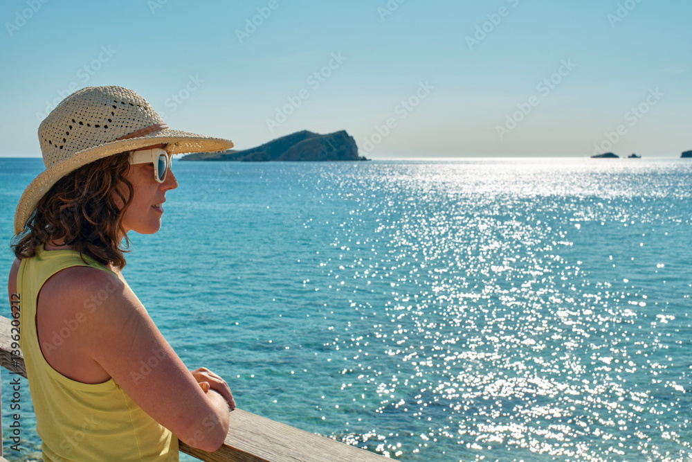 Smiling woman in yellow tank top and sunglasses resting on wooden railing, enjoying the sea view Smiling woman in yellow tank top and sunglasses resting on wooden railing, enjoying the sea view