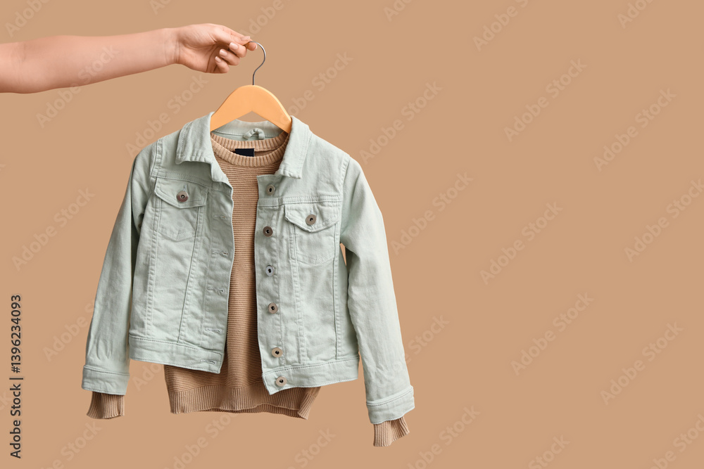 Woman holding hanger with stylish children's clothes on color background
