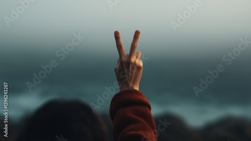 Hand signaling peace against a misty ocean backdrop during twilight hours.