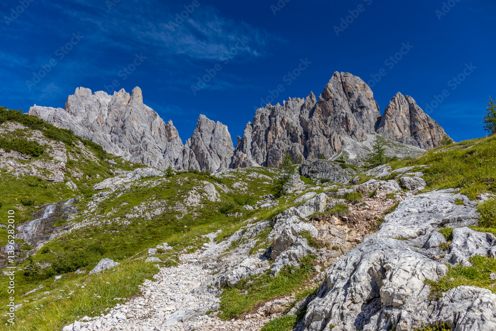 Fototapeta premium Dolomites, Alpi Dolomiti beautiful scenic mountain landscape under blue sky in summer. Rocky tower peak summits of the Alps on a sunny day. Alpine scenic view of the cliffs and climbing walls in Italy