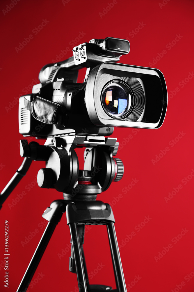 Modern video camera with tripod on red background, closeup