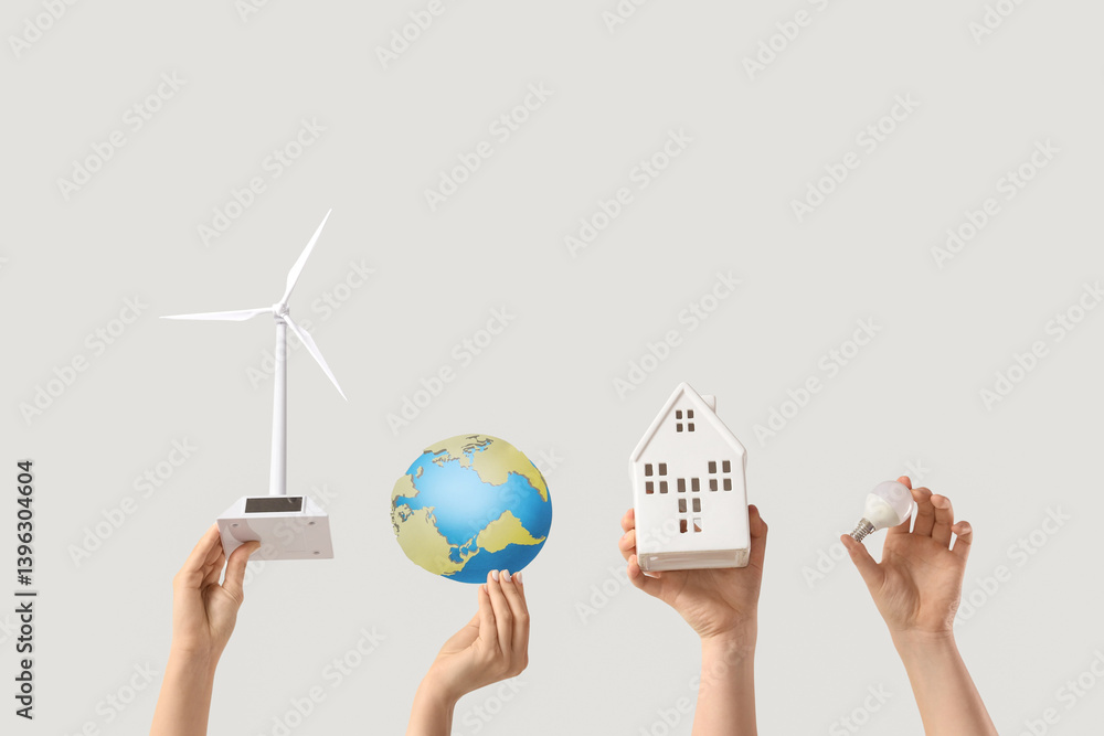 Female hands with wind turbine, house, paper Earth and light bulb on white background. Ecology concept