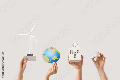 Obraz na płótnie Female hands with wind turbine, house, paper Earth and light bulb on white background. Ecology concept w salonie