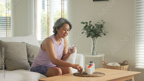Schilderij op canvas Asia adult aged people middle age happy old woman smile drink vitamin d c e k zinc omega 3 fish oil water pill reduce hot flash dry skin health care sit at home sofa elder aging asian