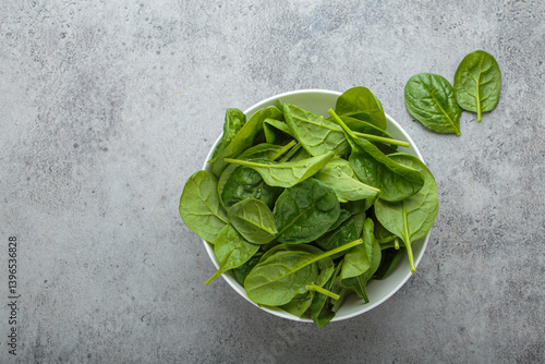 Fresh spinach leaves in a white bowl set on a gray backdrop, showcasing their vibrant green color and healthy appeal, perfect for salads, smoothies, or side dishes. Copy space
