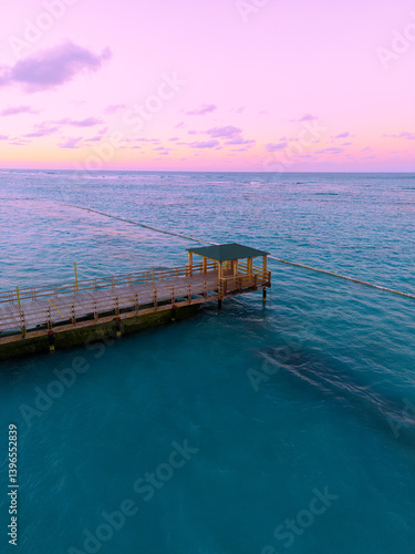 Aerial view of a colorful sunset over the ocean in Punta Cana, with a pier stretching into the water and gentle waves reflecting the fading light. A perfect tropical postcard