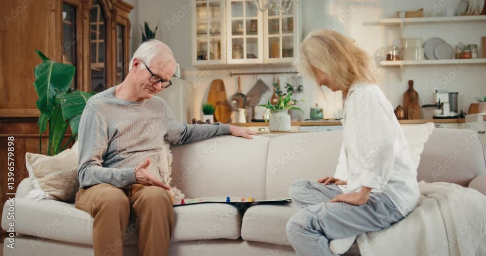 Pastime and leisure of elderly married couple, joyful old woman and her husband. Retirees playing board game at home in weekend, two happy grey-haired people sitting on couch in cozy interior at home Pastime and leisure of elderly married couple, joyful old woman and her husband. Retirees playing board game at home in weekend, two happy grey-haired people sitting on couch in cozy interior at home