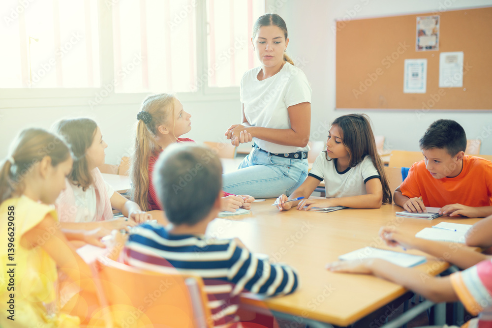 Teacher, together with group of schoolchildren, are looking for solution to complex tasck at round table in a school classroom
