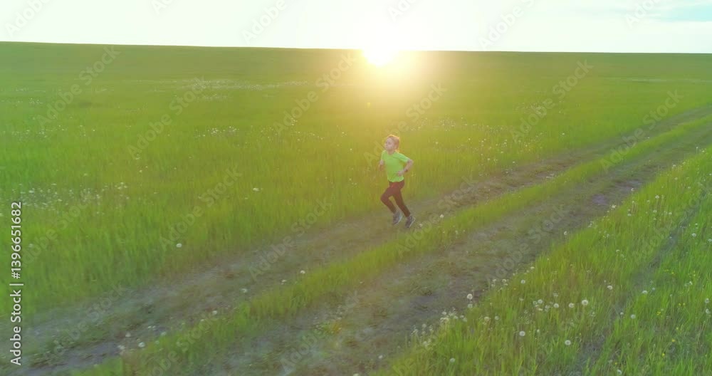 Aerial shoot of a sporty child runs through a wheat field. Evening sport training exercises at rural meadow. A happy childhood is a healthy way of life. Outdoor runing traning. Radial movement, sun Aerial shoot of a sporty child runs through a wheat field. Evening sport training exercises at rural meadow. A happy childhood is a healthy way of life. Outdoor runing traning. Radial movement, sun