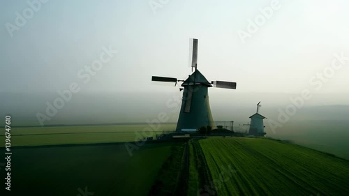 Two windmills stand in a green field under a misty sky, showcasing rural architecture.