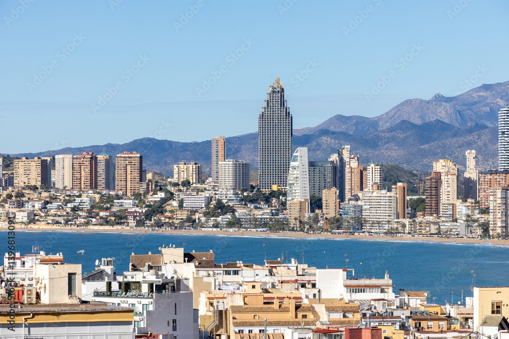 Aerial drone photo over looking the old town of Benidorm in Spain showing apartments and high rise buildings on the Poniente Beach front with the ocean and mountains in the background on a sunny day