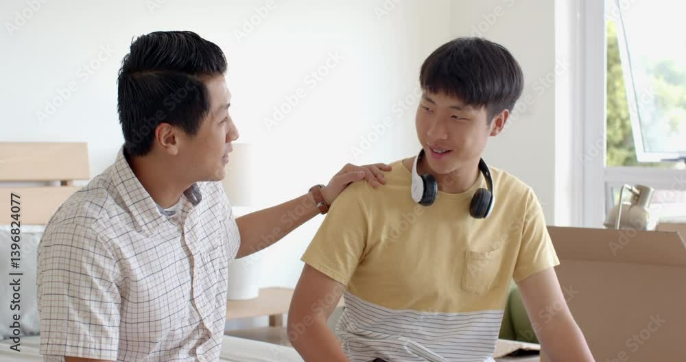 Father congratulating son with car keys gift, both smiling in bedroom Father congratulating son with car keys gift, both smiling in bedroom
