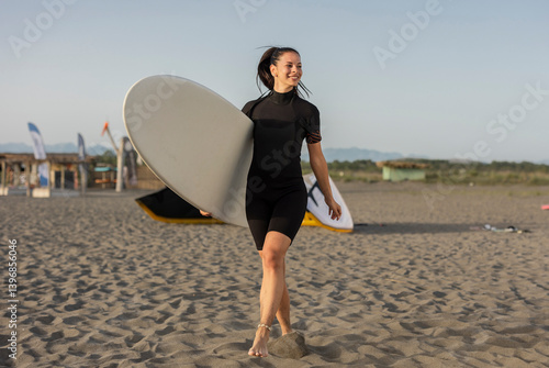 Smiling surfer walking on the beach carrying surfboard
