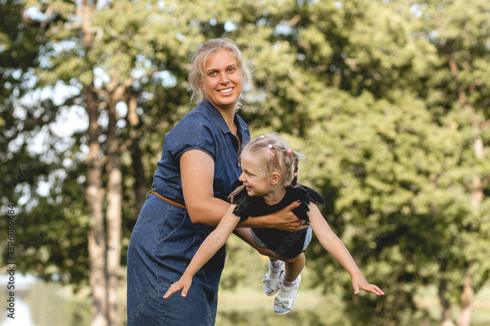 Fototapeta premium Happy mother playing with daughter outdoors, smiling woman holding child in the air in summer park
