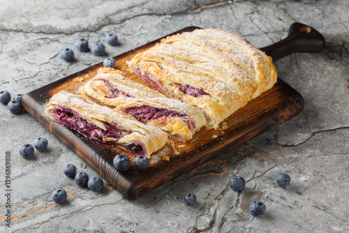 Berry puff pastry pie with blueberries and cream cheese close-up on wooden board on table. Horizontal