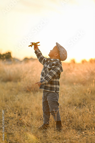 Wallpaper Mural Little boy in a cap and shirt playing with a yellow toy airplane in a golden field at sunset. Dreamy rural childhood moment filled with freedom, imagination, and warm light. Torontodigital.ca