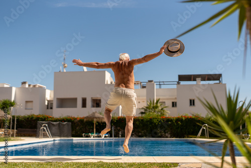 Happy senior man jumping into a pool on a sunny day in Spain, enjoying freedom and active retirement lifestyle photo