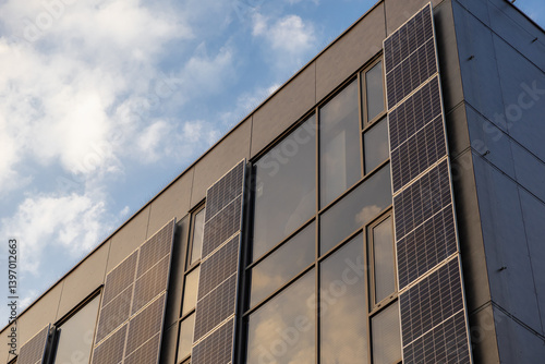 Modern building facade with vertical solar panels and large glass windows reflecting soft evening sky
