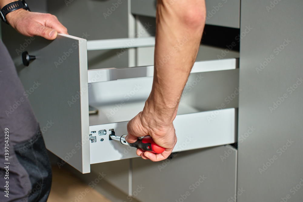 Man assembling kitchen drawer in modern cabinet using screwdriver. Handyman installing and adjusting drawer slide mechanism in contemporary kitchen. Furniture installation