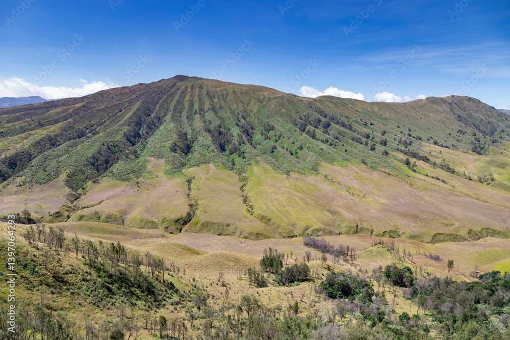 Obraz premium Majestic green mountain with natural ridges and a clear blue sky background. A breathtaking natural landscape perfect for travel, outdoor adventure, and nature conservation projects.