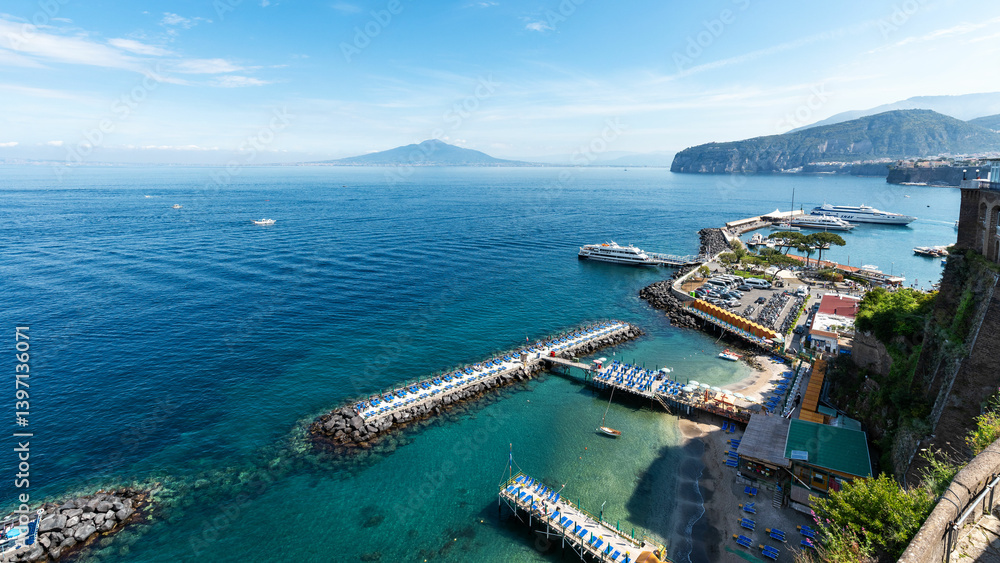 Obraz premium Sorrento, Italy – Stunning panoramic view from the Villa Comunale terrace. The port of Sorrento with its dramatic cliffs and turquoise sea stretches out toward Mount Vesuvius in the distance.