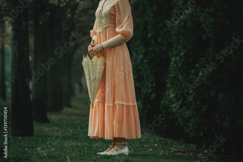 Принти на полотні Peach dress touches wet grass as she waits motionless with closed umbrella, her presence ethereal like memory emerging from forest