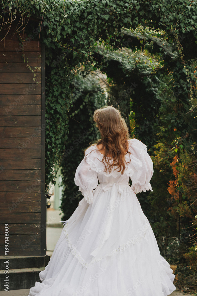 Rear view of young woman in flowing white gown walking away into dark garden path. Concept of vanishing, past lives, spectral femininity. Suitable for ghost romance or gothic fantasy. Rear view of young woman in flowing white gown walking away into dark garden path. Concept of vanishing, past lives, spectral femininity. Suitable for ghost romance or gothic fantasy.