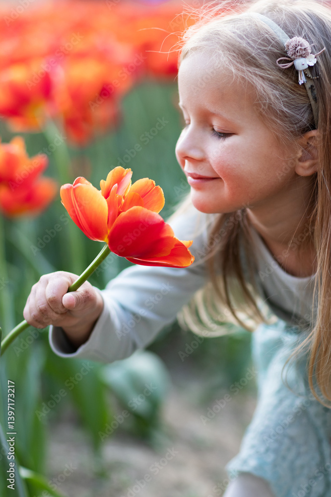 Fototapeta premium Adorable little caucasian blonde girl smiling in tulip field at spring day. Happy children's day 1th of June