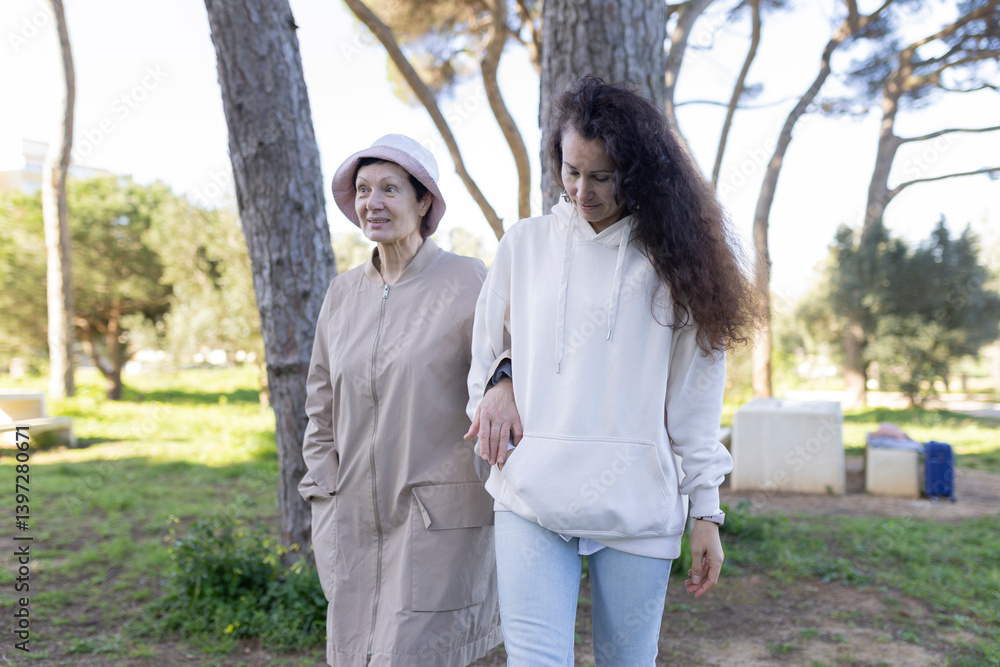 Young woman holding hand of elderly mother while walking in park Young woman holding hand of elderly mother while walking in park
