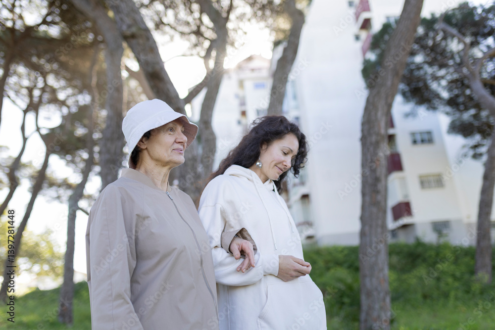Senior woman and her daughter walking in a park, enjoying time together Senior woman and her daughter walking in a park, enjoying time together