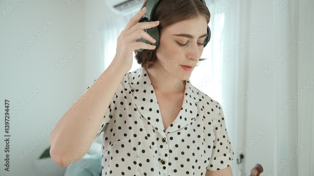 Caucasian mother put on headphone while choosing song by using mobile phone before doing housework. Headset placed on table while was putting on happy housekeeper to listen relaxing song. Pedagogy. Caucasian mother put on headphone while choosing song by using mobile phone before doing housework. Headset placed on table while was putting on happy housekeeper to listen relaxing song. Pedagogy.